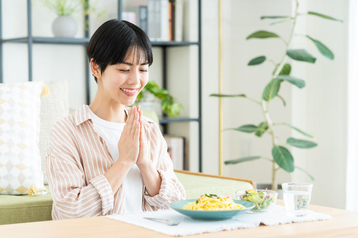 Young Japanese woman eating pasta in her living room (People)