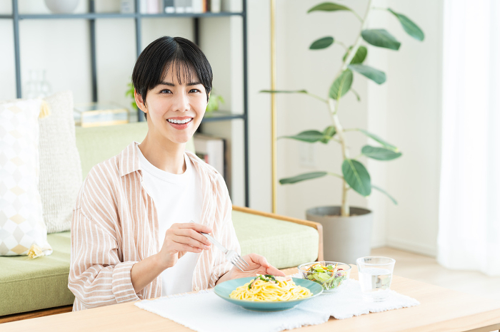 Young Japanese woman eating pasta in her living room (People)