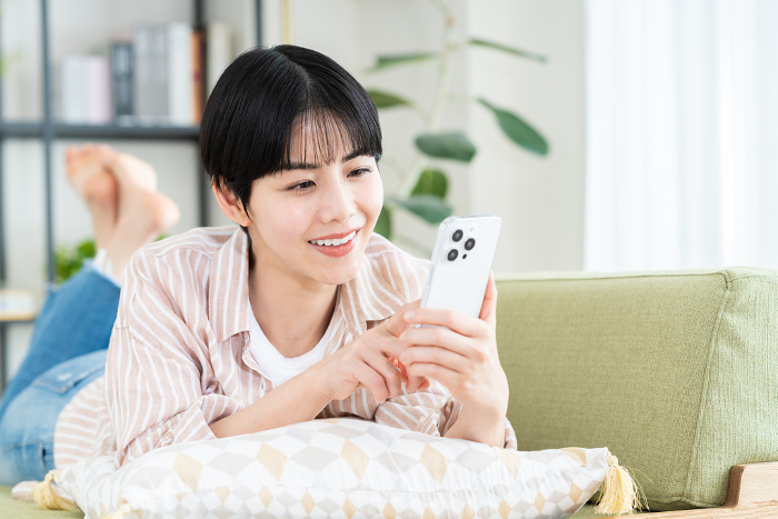 Young Japanese woman looking at her phone in her living room.