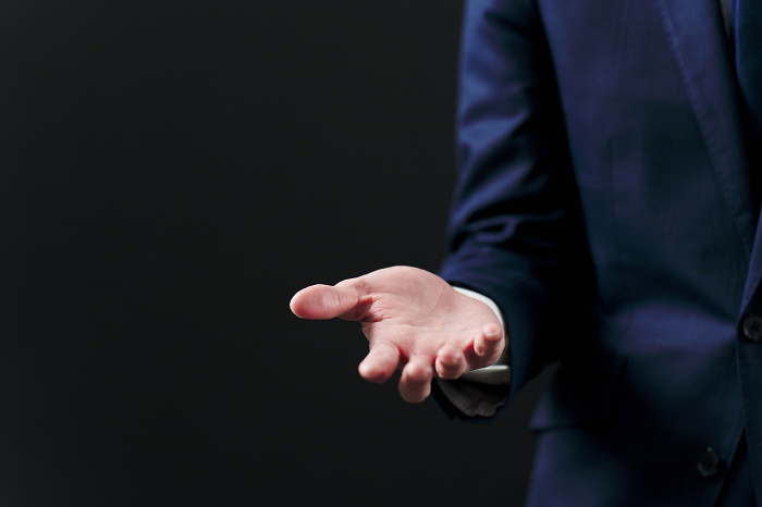 Japanese businessman holding out his hand against black background (People)