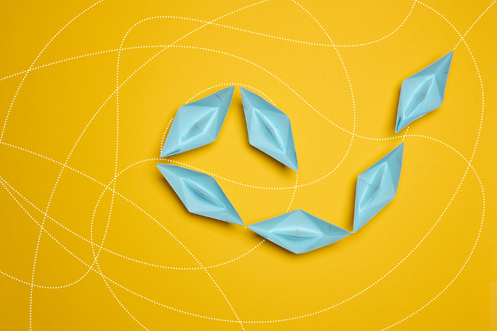 Blue paper boats move one after another on a yellow background, top view Blue paper boats move one after another on a yellow background, top view