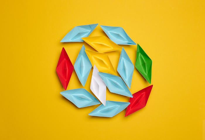 A group of colorful paper boats clustered on a yellow background, top view A group of colorful paper boats clustered on a yellow background, top view