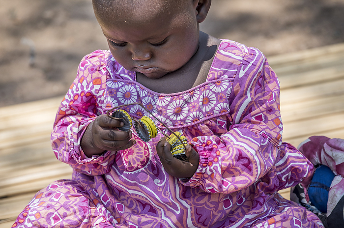 Child playing, Kenya Child playing with a string of bottle tops. Photographed in West Karachuongo, Kaluoch, Homa Bay County, Kenya., by KAREN KASMAUSKI SCIENCE PHOTO LIBRARY