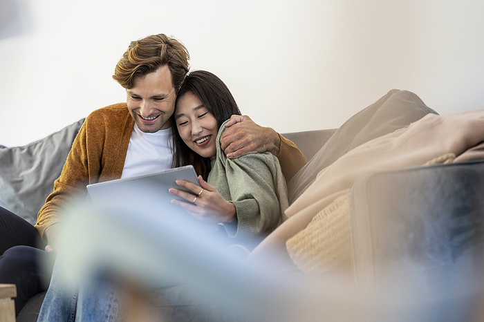 Adult couple snuggled while using digital tablet in living room