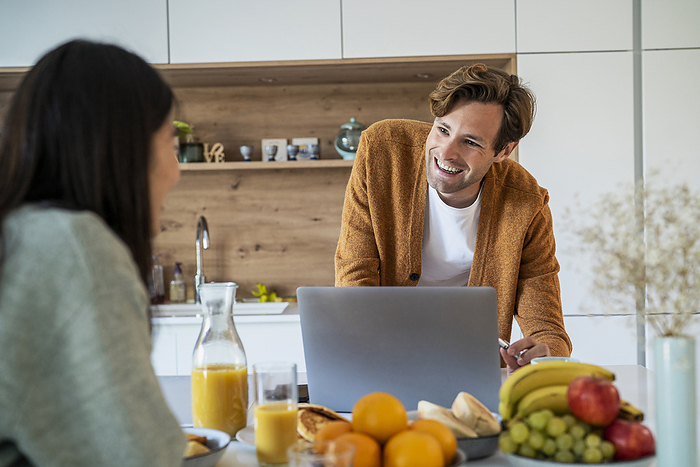 Adult man using laptop while having breakfast with friend