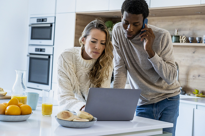 Adult couple using laptop while standing in kitchen