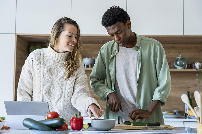 Adult man cutting vegetables at kitchen counter while girlfriend is giving instructions