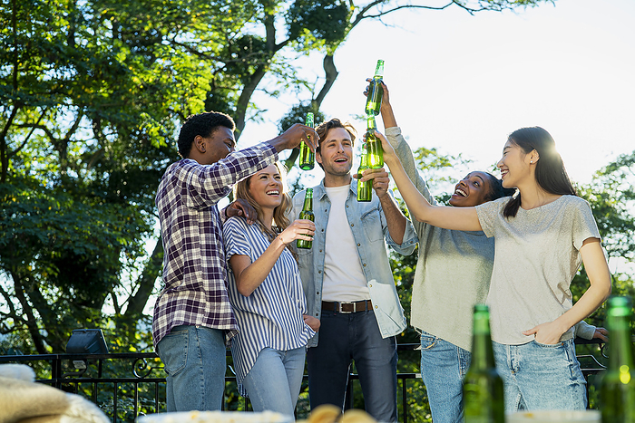 Five friends raising beer bottles while toasting during rooftop party