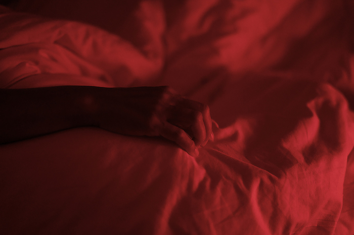 Unidentified person's hand in bed under red light