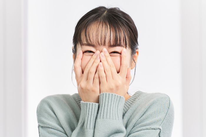 A Japanese woman covers her face with her hands in joy at the surprise.