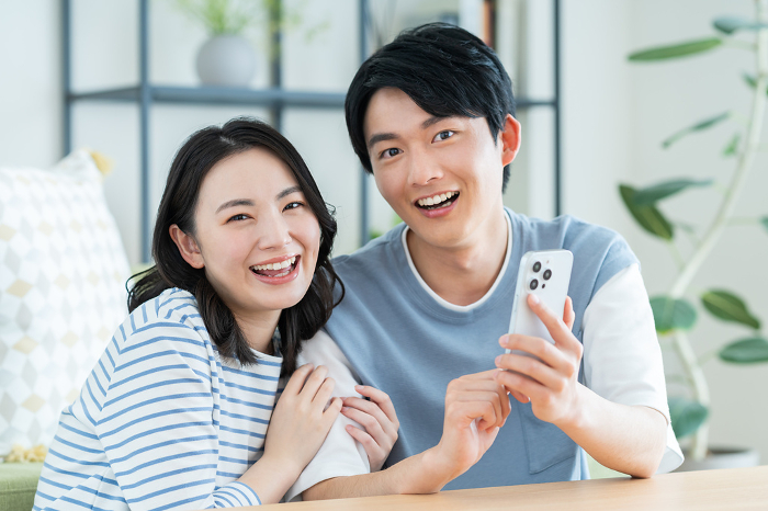 Young Japanese couple looking at a smartphone in their living room (Man & Woman / People)