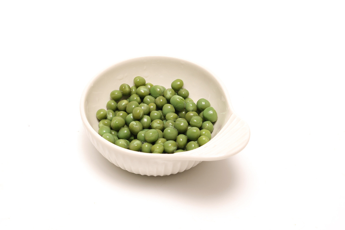 Green peas in a white ceramic bowl on a white background