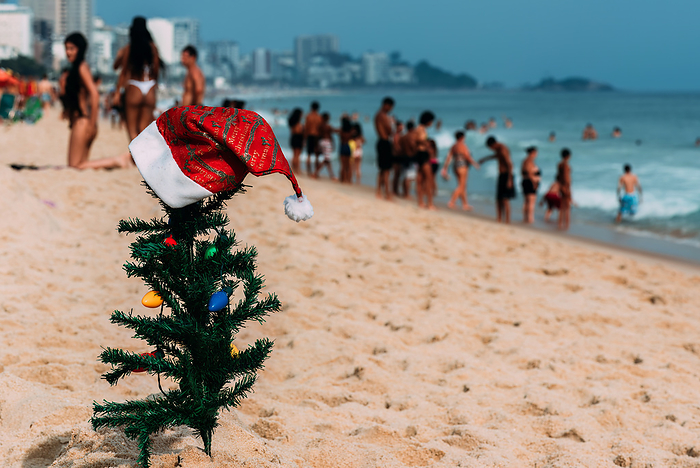 A makeshift small traditional Christmas tree and Santa Claus hat planted on the sand at Leblon Beach in Rio de Janeiro, Brazil with a defocused crowd in the background A makeshift small traditional Christmas tree and Santa Claus hat planted on the sand at Leblon Beach with a defocused crowd in the background, Rio de Janeiro, Brazil, South America, by Alexandre Rotenberg