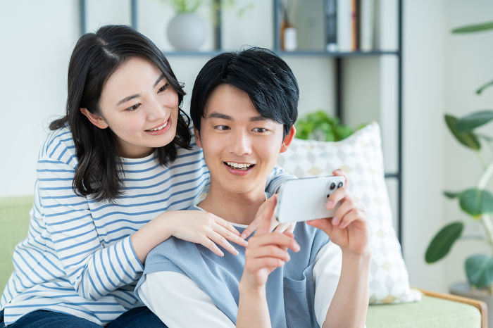 Young Japanese couple looking at their phones in their living room (People)
