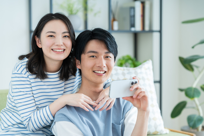 Young Japanese couple looking at their phones in their living room (People)