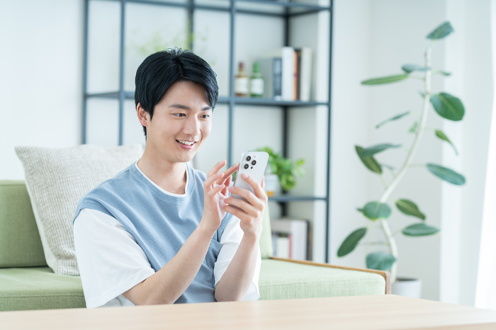 Young Japanese man looking at his phone in his living room.