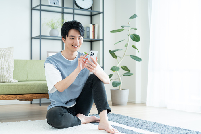 Young Japanese man looking at his phone in his living room.