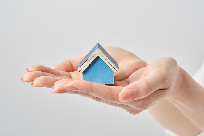 Model of a house placed in the palm of a woman's hand