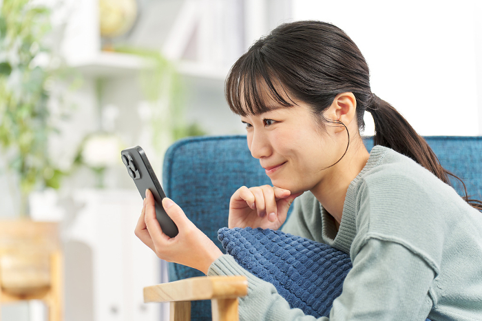 Japanese woman lying on sofa looking at smartphone (People)