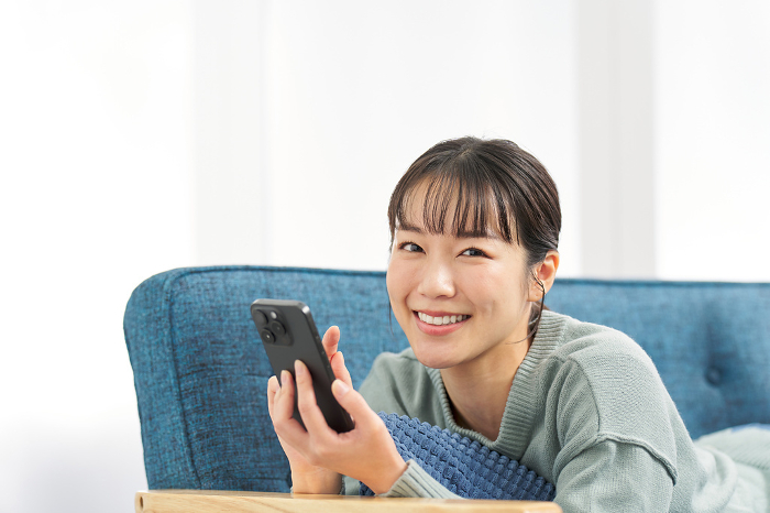 Japanese woman lying on sofa looking at smartphone (People)