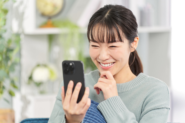 Japanese woman sitting on a sofa looking at her smartphone (People)