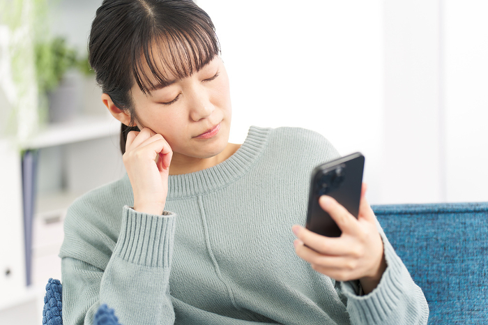 A Japanese woman contemplating while looking at her smartphone (People)