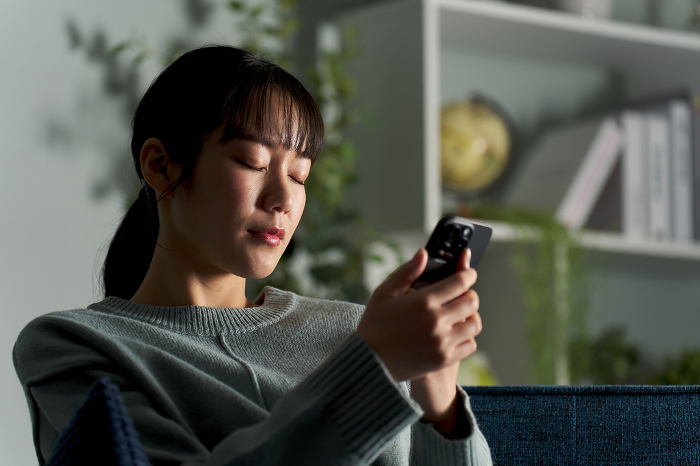 A Japanese woman closes her eyes while looking at her smartphone (People)