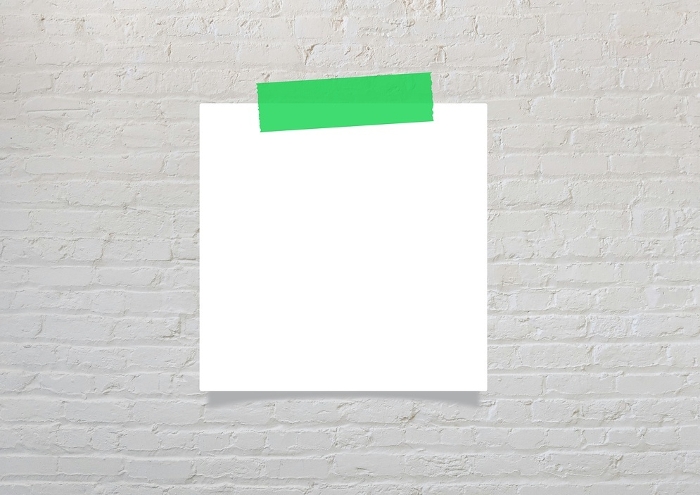 Green masking tape and blank notepaper on gray brick wall
