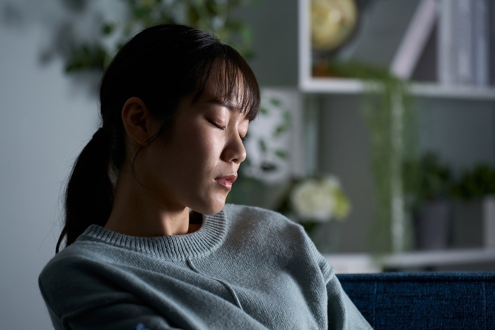 Japanese woman closing her eyes in a dark room.