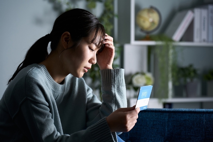 A Japanese woman depressed looking at her bank book in a dark room.