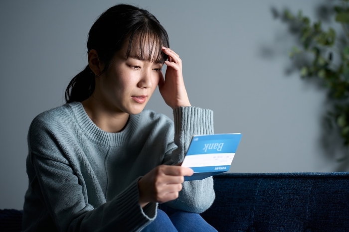 A Japanese woman depressed looking at her bank book in a dark room.