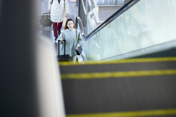 Female inbound foreign tourist climbing escalator with suitcase