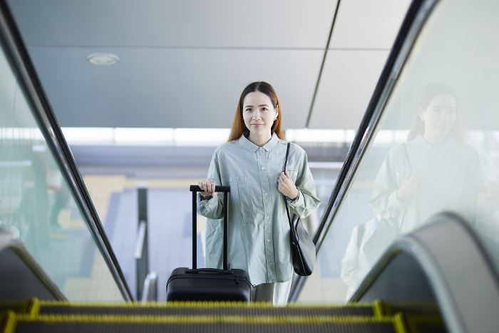 Female inbound foreign tourist climbing escalator with suitcase