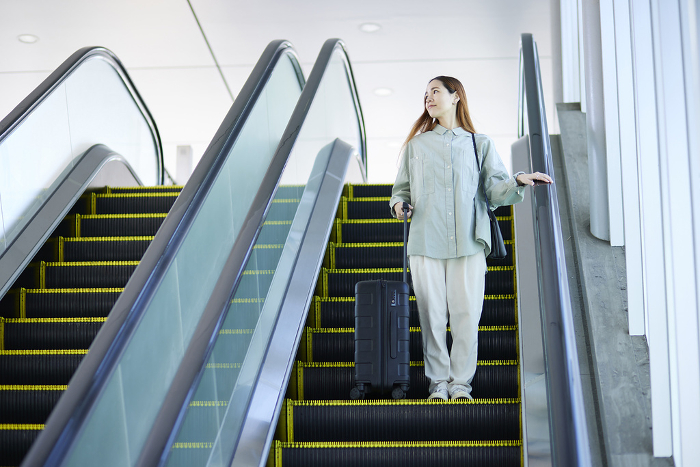 Female inbound foreign tourist going down escalator with suitcase