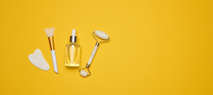 White transparent glass bottle with pipette and roller massager jade on a yellow background. Copy space White transparent glass bottle with pipette and roller massager jade on a yellow background. Copy space