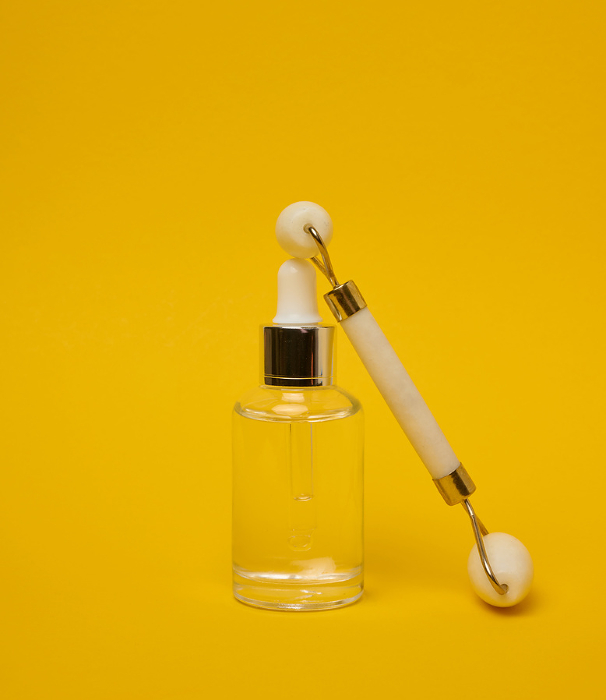 White transparent glass bottle with pipette and roller massager jade on a yellow background White transparent glass bottle with pipette and roller massager jade on a yellow background