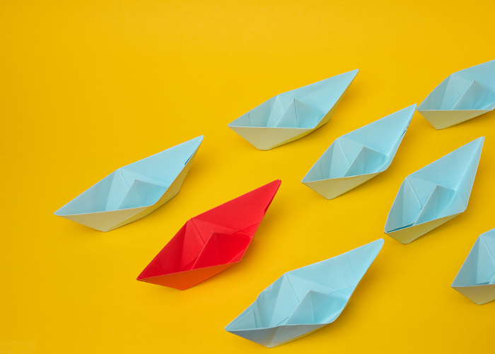 Group of blue paper boats follow red against a yellow background. Strong leader concept, mass manipulation. Starting a business with a well coordinated team, start up Group of blue paper boats follow red against a yellow background. Strong leader concept, mass manipulation. Starting a business with a well coordinated team, start up