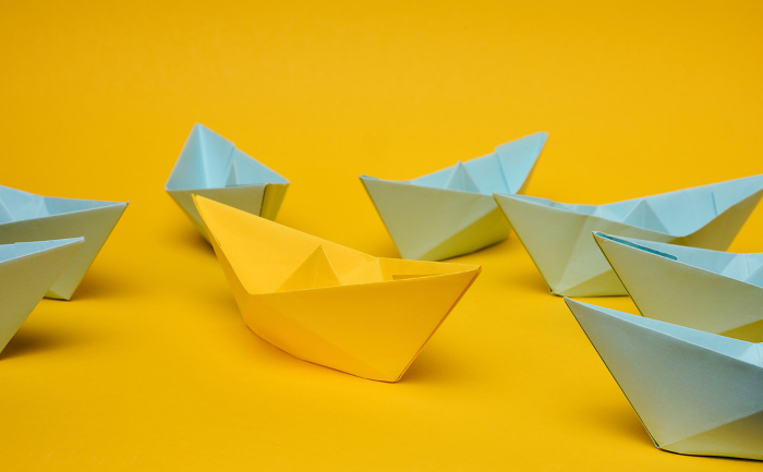 A group of blue paper boats surrounded one yellow boat, the concept of bullying, search for compromise. A group of blue paper boats surrounded one yellow boat, the concept of bullying, search for compromise.