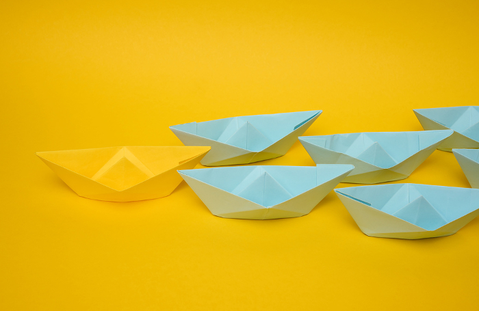 Group of blue paper boats follow yellow against a yellow background. Strong leader concept, mass manipulation. Starting a business with a well coordinated team, start up Group of blue paper boats follow yellow against a yellow background. Strong leader concept, mass manipulation. Starting a business with a well coordinated team, start up