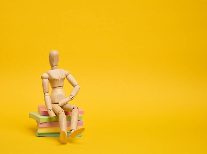 A wooden puppet doll sits on a stack of paper multi colored stickers on a yellow background,  copy space A wooden puppet doll sits on a stack of paper multi colored stickers on a yellow background,  copy space