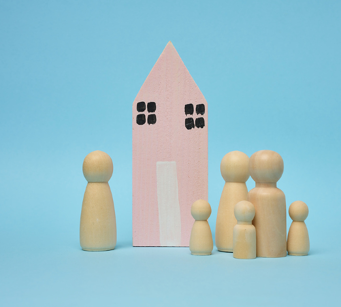 Wooden house and miniature figurines of a family on a blue background. The concept of selling and buying real estate, investment Wooden house and miniature figurines of a family on a blue background. The concept of selling and buying real estate, investment