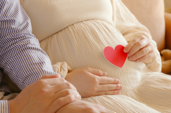 Man and woman holding heart in front of pregnant belly