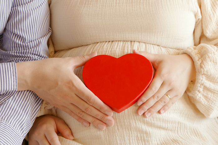 Man and woman holding heart in front of pregnant belly