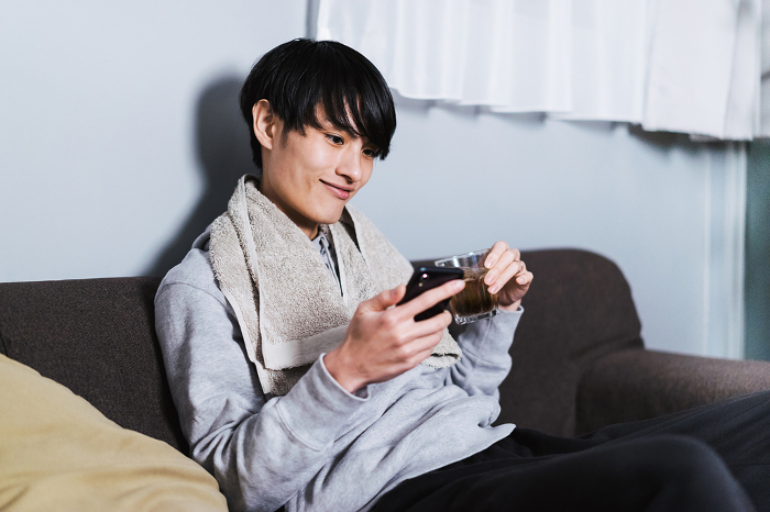 A Japanese man in his 30s operating his smartphone in his room after showering.