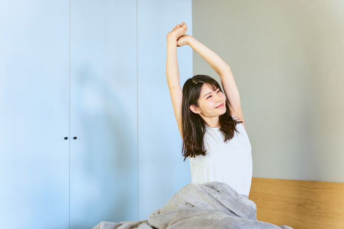 A Japanese woman in her 30s waking up in her bedroom at home, feeling good after waking up from sleep and stretching out her body (People)