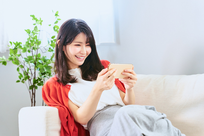 Smiling Japanese woman in her 20s and 30s enjoying watching and viewing videos and reading e-books with her smartphone in landscape orientation (People)