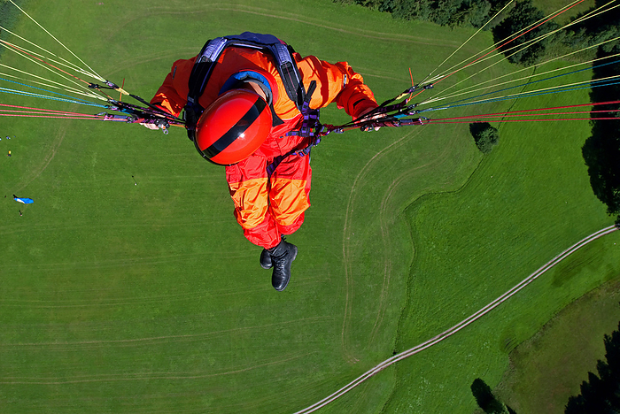 a man in signal red overalls hangs from a paraglider high above the meadows near Lenggries a man in signal red overalls hangs from a paraglider high above the meadows near Lenggries, by Zoonar Andreas Malli