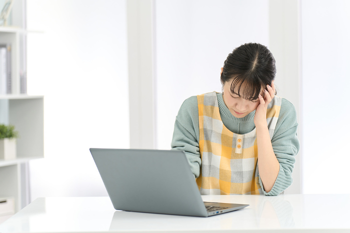 Japanese woman in apron holding her head while working on computer (People)