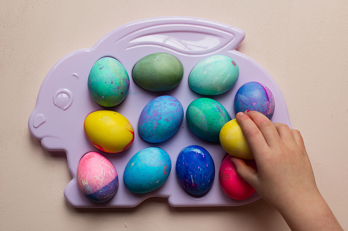 Child reaching for dyed Easter eggs on a plastic tray, by Cavan Images / Lindsay Nolan Photography