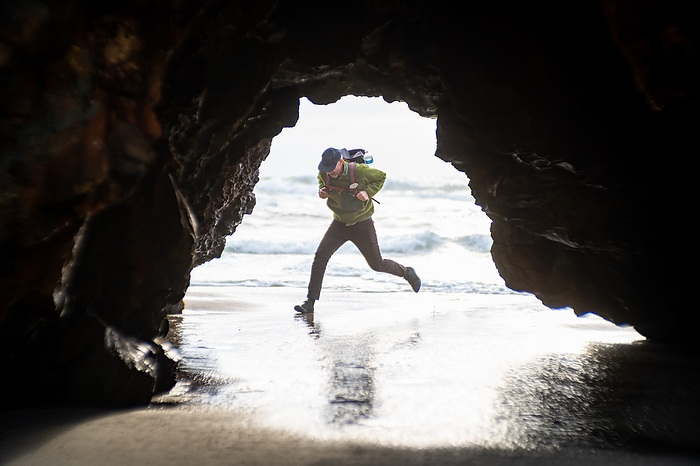 Person running from waves at beach holding onto backpack, by Cavan Images / Christian Ericksen